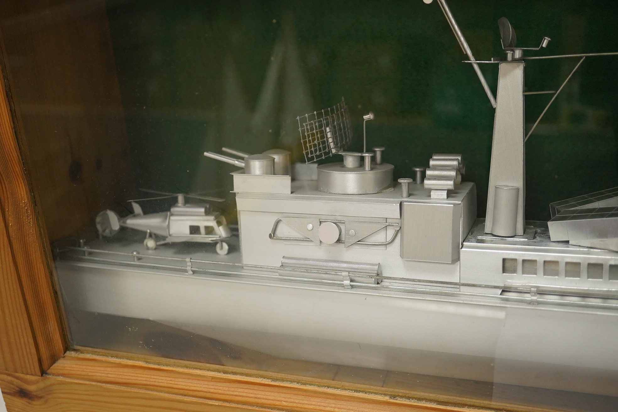 A pine cased aluminium model of a naval frigate, hull 86cm long, display case 96.5 x 18 x 36cm. Condition - good.